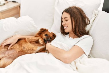 Genç İspanyol kadın yatak odasında köpeğe sarılıyor.