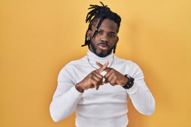 Sarı arka plan reddedilmesinin üzerine balıkçı yaka kazak giyen Afrikalı bir adam negatif işaret veriyor. 