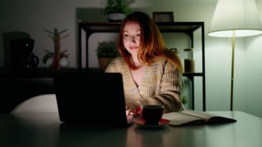 Young redhead woman using laptop studying at home