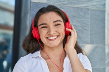 Genç İspanyol kadın sokakta müzik dinlerken kendinden emin gülümsüyor.