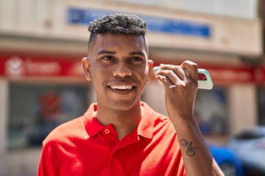 Genç Latin adam gülümsüyor. Caddedeki akıllı telefondan kendine güvenen bir sesli mesaj dinliyor.