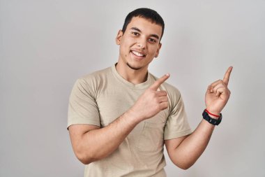 Young arab man wearing casual t shirt smiling and looking at the camera pointing with two hands and fingers to the side. 