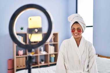 Koyu renk saçlı İspanyol bir kadın akıllı telefonuyla güzellik dersi kaydediyor. Olumlu ve mutlu görünüyor. Kendine güvenen bir gülümsemeyle dişlerini gösteriyor. 