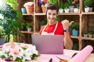 Çiçekçide çalışan genç İspanyol bir adam video çekiyor. Başparmağıyla işaret ediyor. Ağzı açık gülümsüyor. 