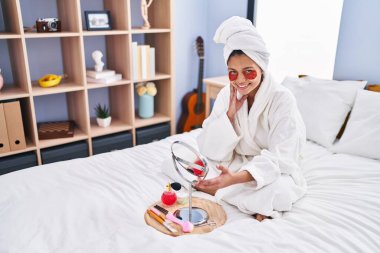 Genç Latin kadın, yatakta uzanmış, dolgun göz tedavisi görüyor.