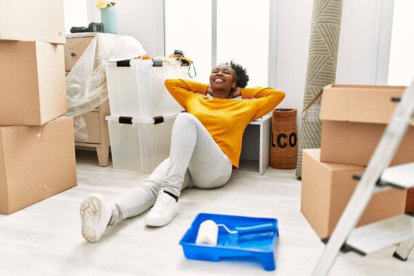 Африканская американка сидит на полу расслабленный с руками на голове в новом доме