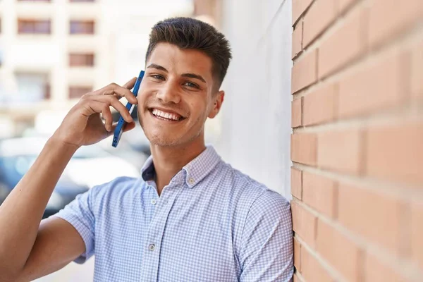 若いヒスパニック系の男が路上でスマートフォンで自信を持って話して笑っている — ストック写真
