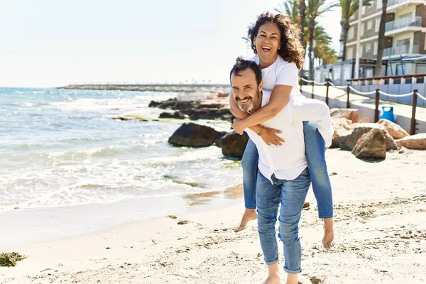 Hombre Hispano Mediana Edad Sonriendo Feliz Sosteniendo Mujer Espalda Playa —  Fotos de Stock