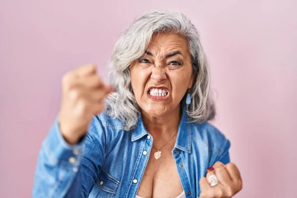 ピンク色の背景に白髪の中年女性が怒って怒って怒って怒って叫んでいる間に拳を上げ 激怒しました 怒りと攻撃的な考え方 — ストック写真