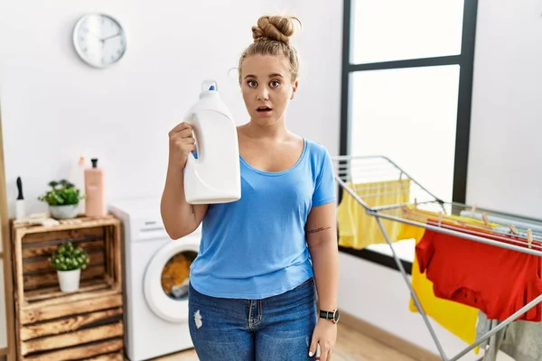 Young Caucasian Woman Holding Detergent Bottle Laundry Room Scared Amazed — Zdjęcie stockowe