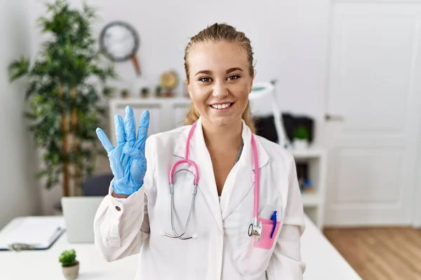 在诊所里 身穿医生制服和听诊器的年轻的高加索女人带着自信和快乐的微笑 展示并指点着4号手指 — 图库照片