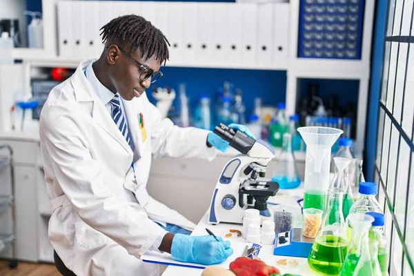 Cientista Homem Afro Americano Usando Microscópio Escrevendo Relatório Laboratório — Fotografia de Stock