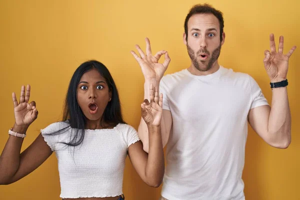 Interracial Couple Standing Yellow Background Looking Surprised Shocked Doing Approval — Foto Stock