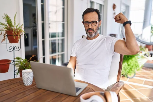 Middle age man using computer laptop at home strong person showing arm muscle, confident and proud of power