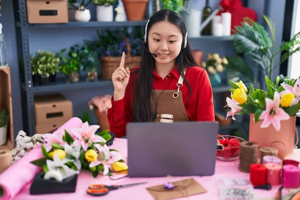 Young asian woman working at florist shop doing video call smiling with an idea or question pointing finger with happy face, number one