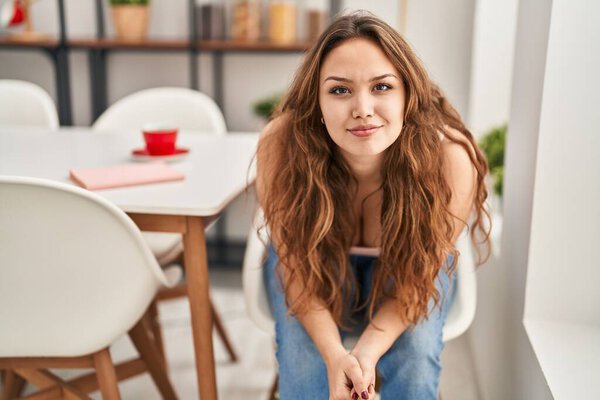 Young beautiful hispanic woman smiling confident sitting on chair at home
