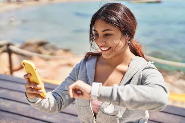 Młoda Latynoska Kobieta Ubrana Stoperek Sportowy Używająca Smartfona Nad Morzem — Zdjęcie stockowe