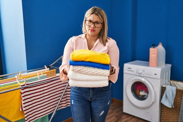 Young Hispanic Woman Holding Folded Laundry Ironing Skeptic Nervous Frowning — Stockfoto