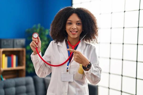 Young african american doctor woman wearing doctor uniform and stethoscope smiling happy pointing with hand and finger