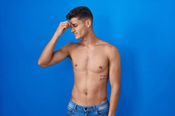 Young hispanic man standing shirtless over blue background tired rubbing nose and eyes feeling fatigue and headache. stress and frustration concept.