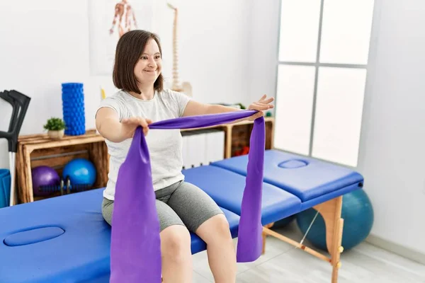 Brunette woman with down syndrome traning arms resistance with elastic bands at physiotherapy clinic