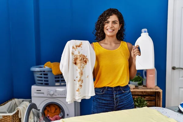Young Latin Woman Holding Dirty Shirt Detergent Bottle Laundry Room — Stockfoto