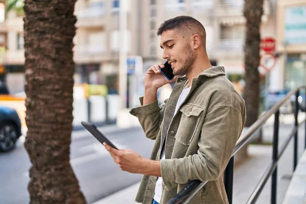 Young Hispanic Man Talking Smartphone Using Touchpad Street — Zdjęcie stockowe