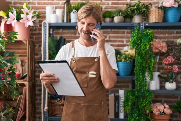 Young Blond Man Florist Talking Smartphone Reading Clipboard Flower Shop — Stock Photo, Image