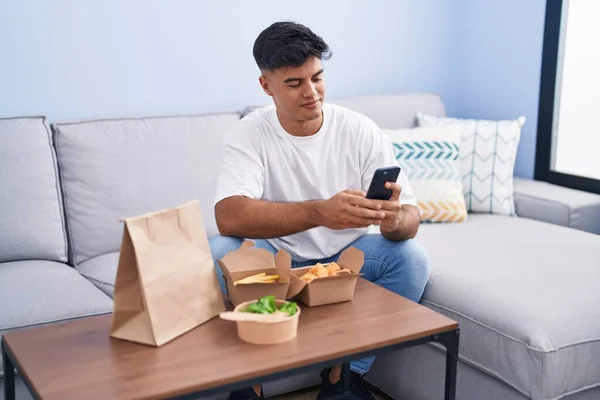 Junger Hispanischer Mann Isst Hause Mit Smartphone Essen Zum Mitnehmen — Stockfoto