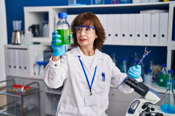 Μέση Ηλικία Γυναίκα Επιστήμονας Κρατώντας Μπουκάλι Έγγραφο Ανάγνωσης Στο Εργαστήριο — Φωτογραφία Αρχείου
