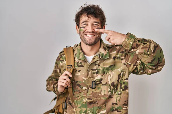 ヒスパニック系の若い男が顔や鼻に手指を指してカモフラージュ軍の制服を着て 陽気な笑顔 美の概念 — ストック写真