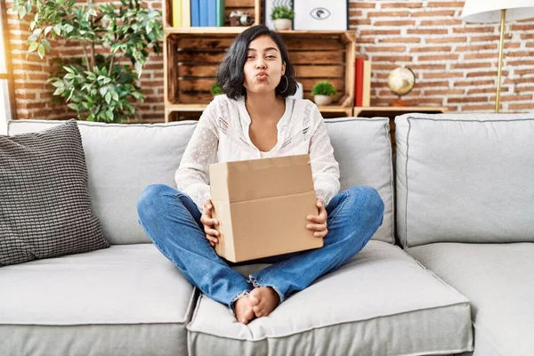 Young hispanic woman sitting on the sofa checking delivery package looking at the camera blowing a kiss being lovely and sexy. love expression.