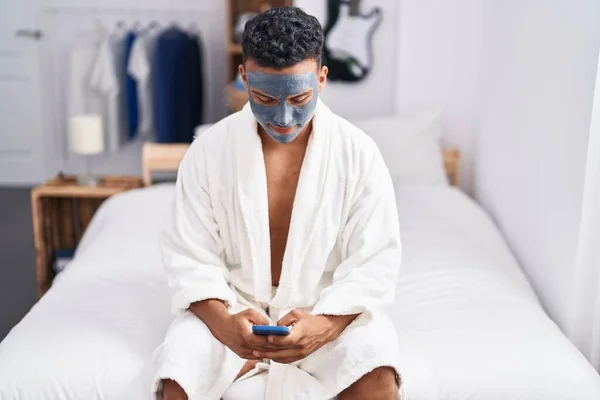 Mladý Latinský Muž Uvolněný Posteli Ošetření Obličejové Masky Pomocí Smartphone — Stock fotografie