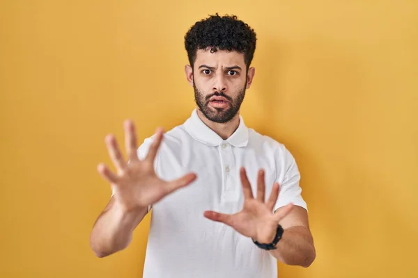 黄色の背景の上に立っているアラブの男は恐れていると手で恐怖の表現を停止ジェスチャーを恐れて 衝撃で叫んでいる パニックの概念 — ストック写真
