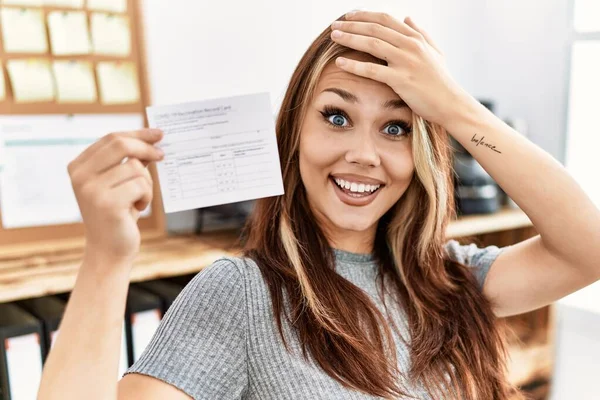 Young caucasian woman holding covid record card stressed and frustrated with hand on head, surprised and angry face