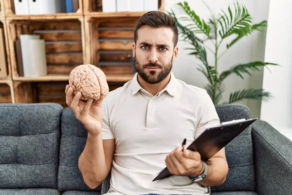 Handsome Hispanic Man Holding Brain Working Psychology Clinic Skeptic Nervous — Zdjęcie stockowe