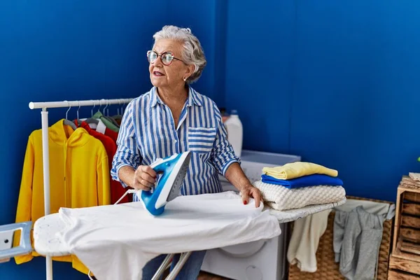 シニア白髪の女性が洗濯室で自信を持ってアイロンをかける — ストック写真