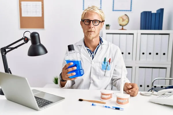 Young Blond Dentist Man Holding Mouthwash Clinic Thinking Attitude Sober — Foto Stock