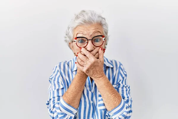 Senior woman with grey hair standing over white background shocked covering mouth with hands for mistake. secret concept.