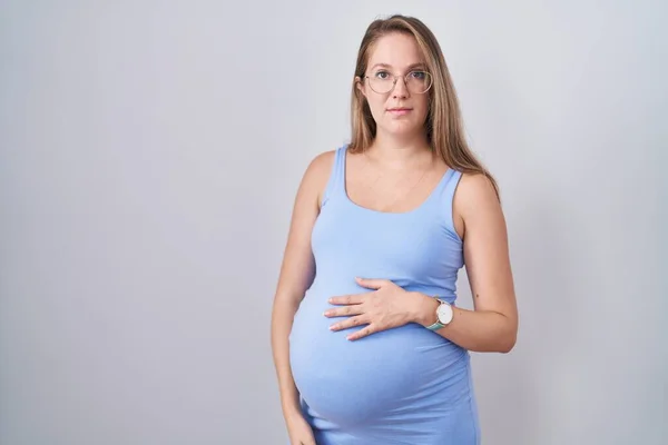 Jonge Zwangere Vrouw Staat Witte Achtergrond Ontspannen Met Serieuze Uitdrukking — Stockfoto