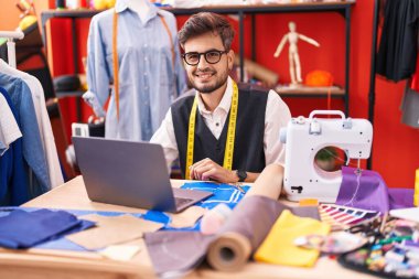 Genç İspanyol terzi atölyede dizüstü bilgisayar kullanarak gülümsüyor.