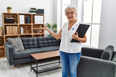 Psikoloji merkezinde elinde dosya tutan yaşlı, gri saçlı bir kadın psikolog.