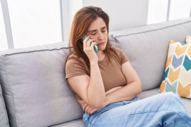 Evdeki koltukta oturmuş akıllı telefondan konuşan genç bir kadın.