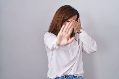 Esmer kadın, izole edilmiş beyaz arka planda duruyor. Gözleri ellerle kaplıyor ve üzgün ve korku dolu bir ifadeyle dur hareketi yapıyor. utangaç ve olumsuz kavram. 