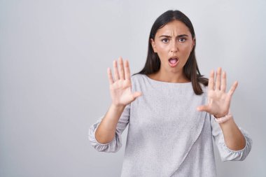 Young hispanic woman standing over white background doing stop gesture with hands palms, angry and frustration expression 