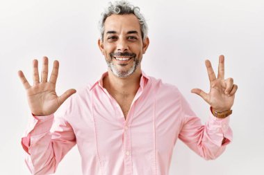 Orta yaşlı İspanyol adam izole edilmiş arka planda duruyor. Sekiz numaralı parmaklarıyla işaret ediyor ve gülümsüyor. Kendinden emin ve mutlu.. 