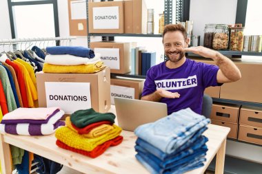Gönüllü tişört giyen orta yaşlı bir adam. Dizüstü bilgisayarla çalışıyor. Ellerinde büyük boy ve ölçü işareti var. Kameraya bakıp gülümsüyor. ölçüm kavramı. 