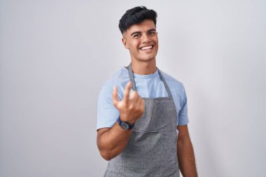 Beyaz arka plan üzerine önlük giymiş İspanyol genç adam seni buraya davet ediyor. Elinle mutlu bir şekilde karşıla ve gülümse. 