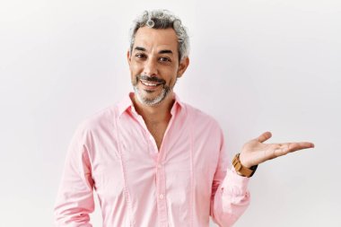 Orta yaşlı, ispanyol bir adam izole edilmiş arka planda durup neşeli bir şekilde sunum yapıyor ve avuç içi kameraya bakıyor.. 