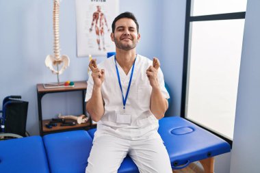 Sakallı, sakallı, klinikte çalışan, umut ve gözlerin kapalı gülümseyerek el hareketi yapan genç bir İspanyol. Şans ve batıl inançlar. 